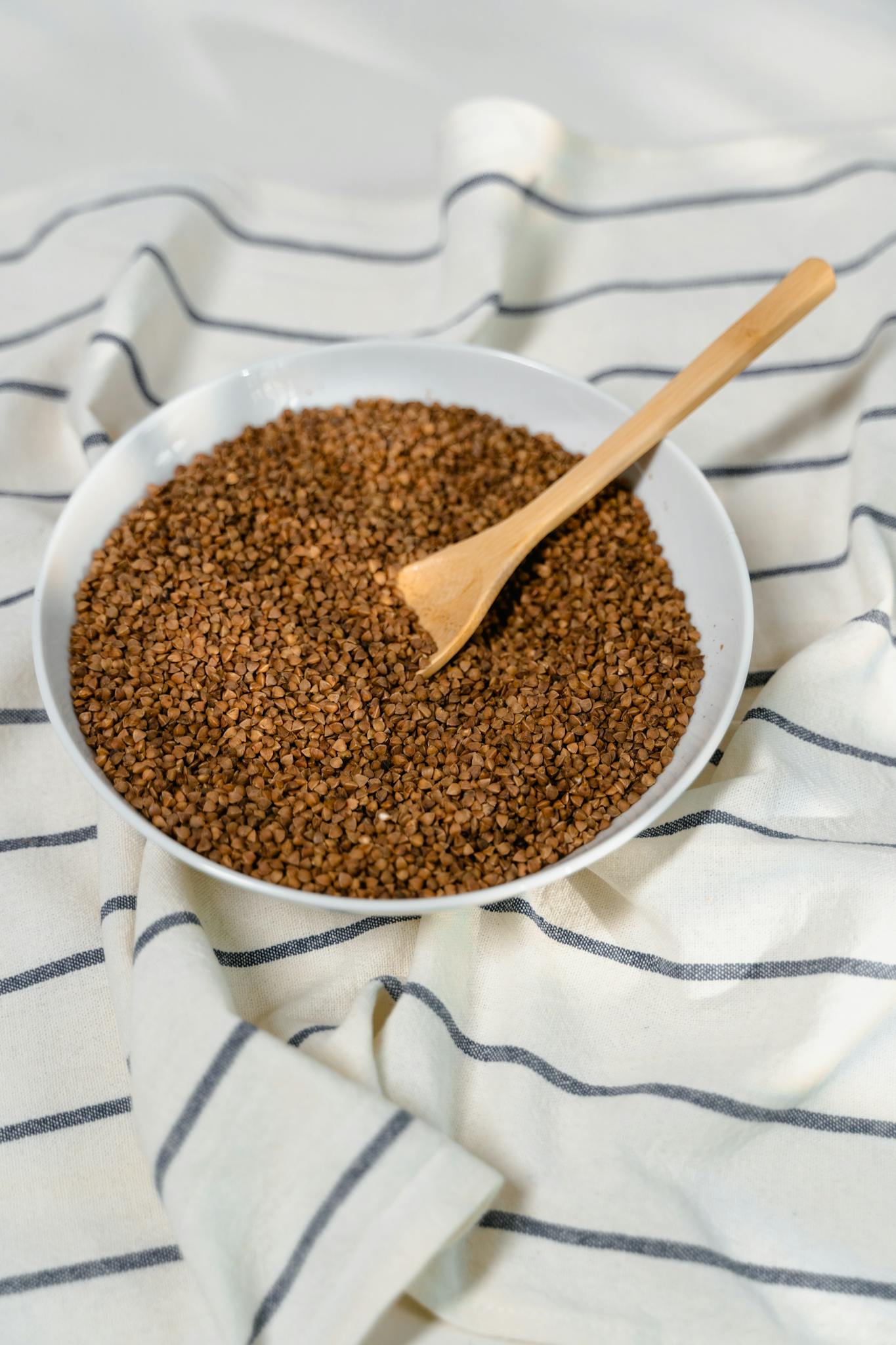 A bowl of instant coffee granules with a wooden spoon on a striped fabric backdrop.