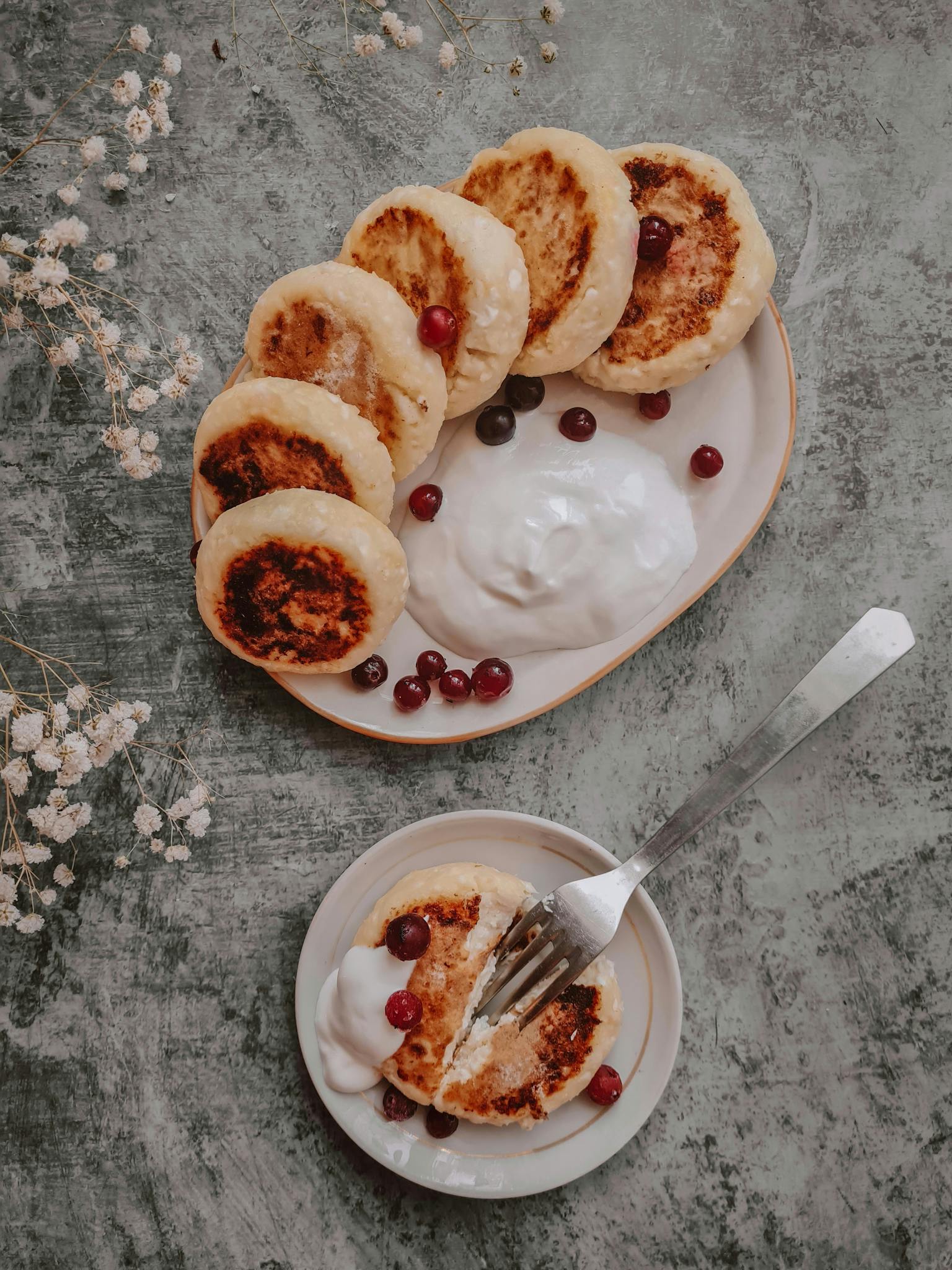 Delicious rustic pancakes served with cream and cranberries on a stone table.